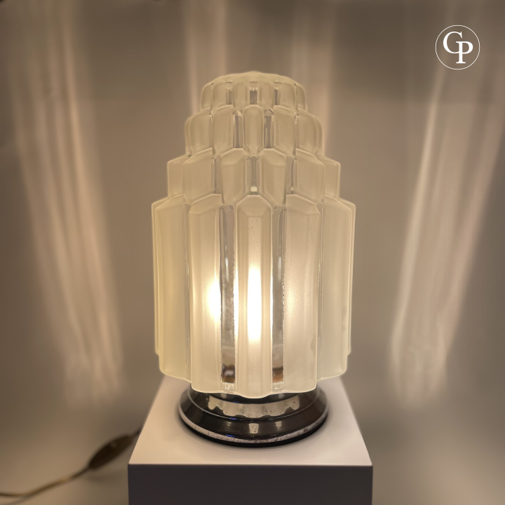 Vintage Art Deco "Skyscraper" table lamp glowing with warm light, showcasing its iconic tiered frosted glass shade and chrome base | Lampe de table vintage Art Déco "Skyscraper" allumée diffusant une lumière chaude, mettant en valeur son abat-jour iconique en verre dépoli à étages et sa base chromée