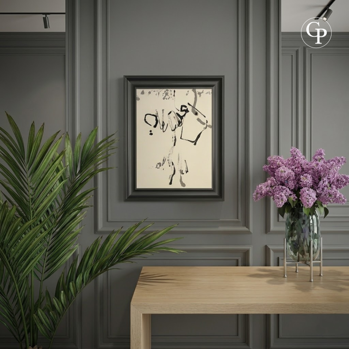 Encre abstraite Élan Lyrique de Hanna Ben-Dov encadrée dans un cadre noir épuré, fixée sur un mur à moulures gris anthracite au-dessus d'une console en bois clair, avec un vase de lilas violets et une plante verte. | Framed abstract ink Lyrical Impulse by Hanna Ben-Dov in a sleek black frame, hanging on a charcoal grey paneled wall above a light wood console table, styled with a vase of purple lilacs and a green plant.