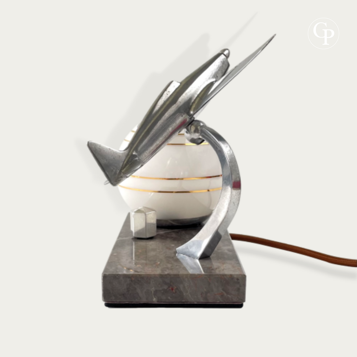 Side view of an Art Deco airplane table lamp showing the chrome fuselage, striped glass globe, and marble base thickness | Vue de profil d'une lampe de table avion Art Déco montrant le fuselage chromé, le globe en verre rayé et l'épaisseur du socle en marbre
