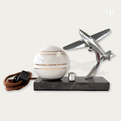 Art Deco table lamp featuring a chrome airplane and white glass globe with gold stripes on a marble base | Lampe de table Art Déco avec avion en chrome et globe en verre blanc à liserés dorés sur socle en marbre