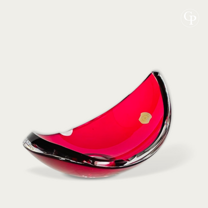 Vue de trois-quarts du vide-poche moderniste en cristal doublé rouge rubis de René Delvenne pour Val Saint Lambert, étiquette d'origine visible | Three-quarter view of the Mid-Century modern ruby red cased crystal vide-poche bowl by René Delvenne for Val Saint Lambert, showing the original label.