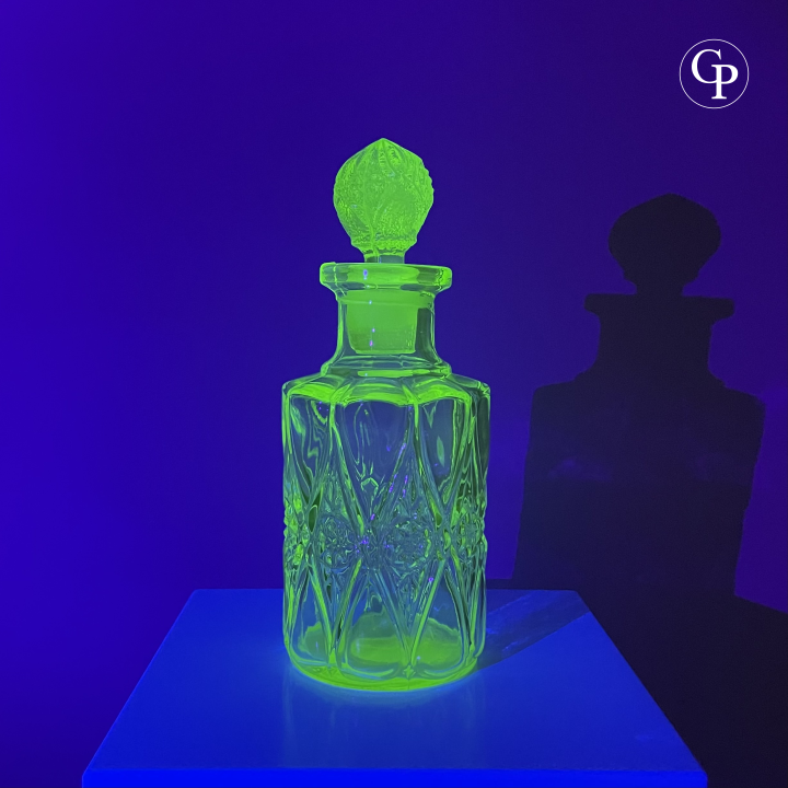 Spectacular view of the Val Saint Lambert Ouraline uranium glass perfume bottle glowing intense neon green under UV light, highlighting its authentic uranium content, Art Deco circa 1935. | Vue spectaculaire du flacon Val Saint Lambert en verre à l'uranium Ouraline illuminé d'un vert néon intense sous lumière UV, mettant en évidence son authentique teneur en uranium, Art Déco vers 1935.