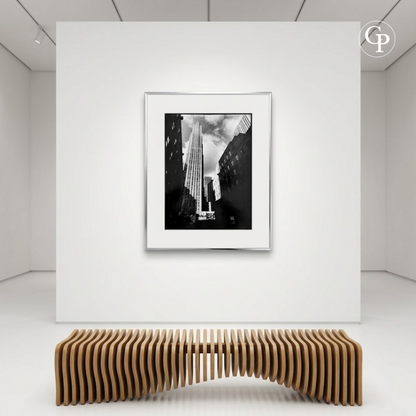 Mise en situation dans une galerie d'art contemporaine de la photographie Rockefeller Center de Michel Pinel, encadrée au-dessus d’un banc en bois design. | Gallery room showcasing the framed black and white photography Rockefeller Center by Michel Pinel hanging on a wall above a modern wooden bench.