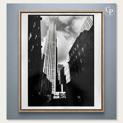 Photographie d’art en noir et blanc Rockefeller Center de Michel Pinel, tirage argentique original de 1986 présenté dans un cadre élégant en bois naturel clair sur un fond bleu gris. | Black and white art photography Rockefeller Center by Michel Pinel, original 1986 silver gelatin print displayed in an elegant light natural wood frame against a blue-grey background.
