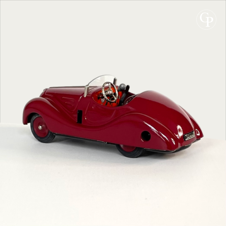 Rear three-quarter view of the deep red Schuco Examico 4001 vintage tinplate roadster, showing the cockpit with steering wheel, gear lever, and the Schuco logo on the rear license plate. | Vue arrière de trois-quarts d'une voiture automate Schuco Examico 4001 bordeaux, mettant en valeur l'habitacle avec son volant, le levier de vitesse et l'inscription Schuco à l'arrière.