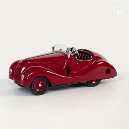 Three-quarter side profile view of a deep red Schuco Examico 4001 vintage tinplate roadster toy car, showcasing its aerodynamic 1930s BMW 328 inspired lines on a light background. | Vue de profil de trois-quarts d'une voiture automate Schuco Examico 4001 de couleur bordeaux, soulignant ses lignes aérodynamiques inspirées de la BMW 328 des années 1930 sur fond clair.